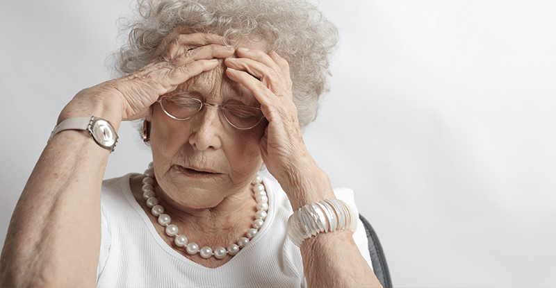 Stará pani s bielymi vlasmi a okuliarmi sa drží za hlavu od bolesti a trápenia