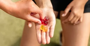 Konopné gumené cukríky - natiahnutá dlaň s gumenými cukríkmi a ruka, ktorá sa po nich naťahuje