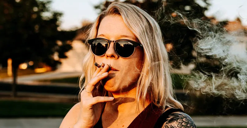 Mladá žena v slnečných okuliaroch fajčí jointa