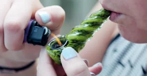 Detail zapaľovania zelenej pyrexovej fajky, naplnenej marihuanou a priloženej k ženským ústam