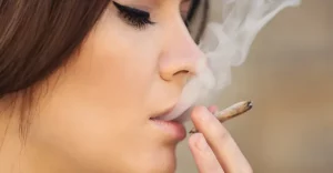 Mladá žena vyfukuje dym z jointa - detail